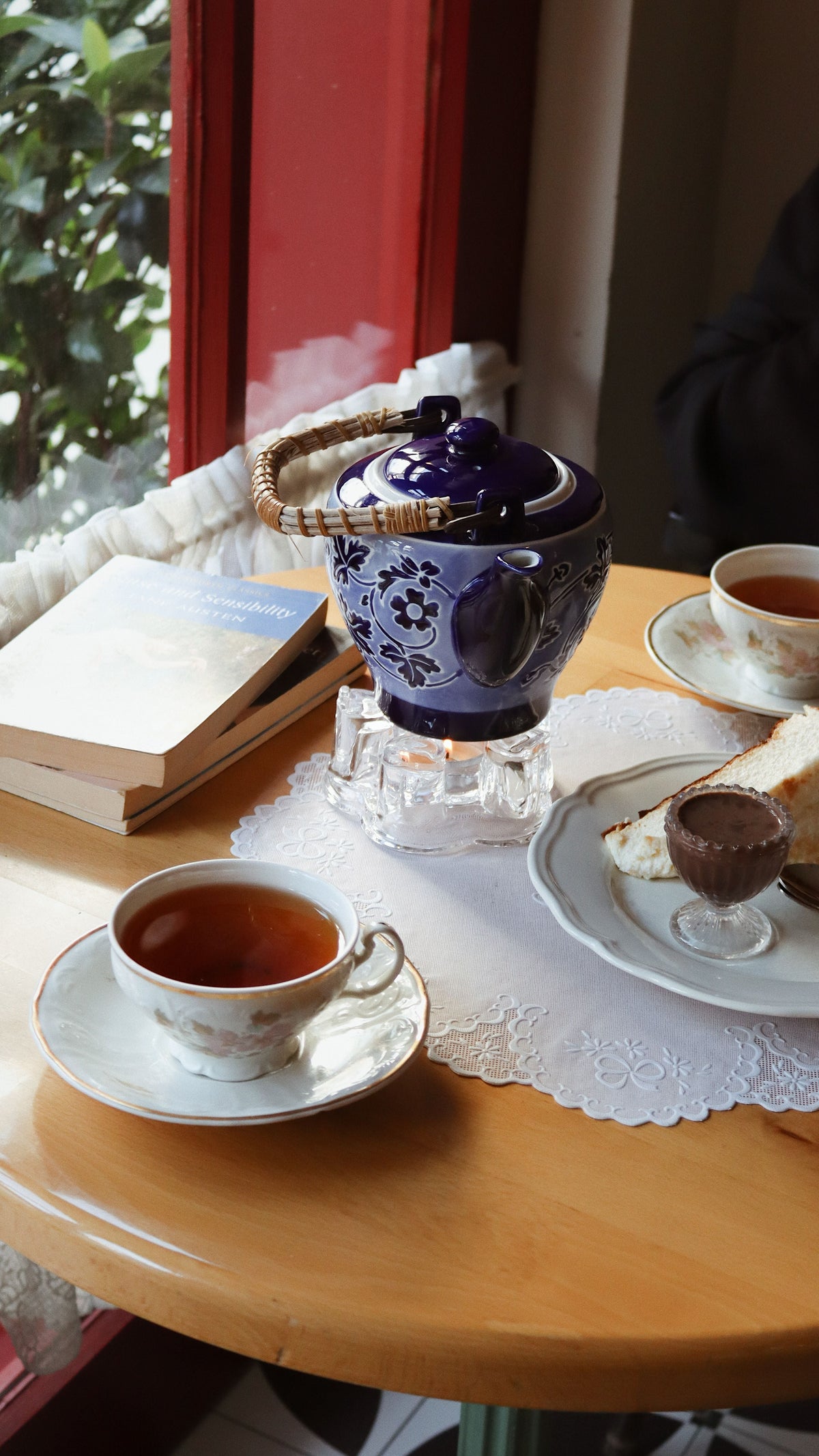 A blue teapot and cups of tea beside books on a wooden table