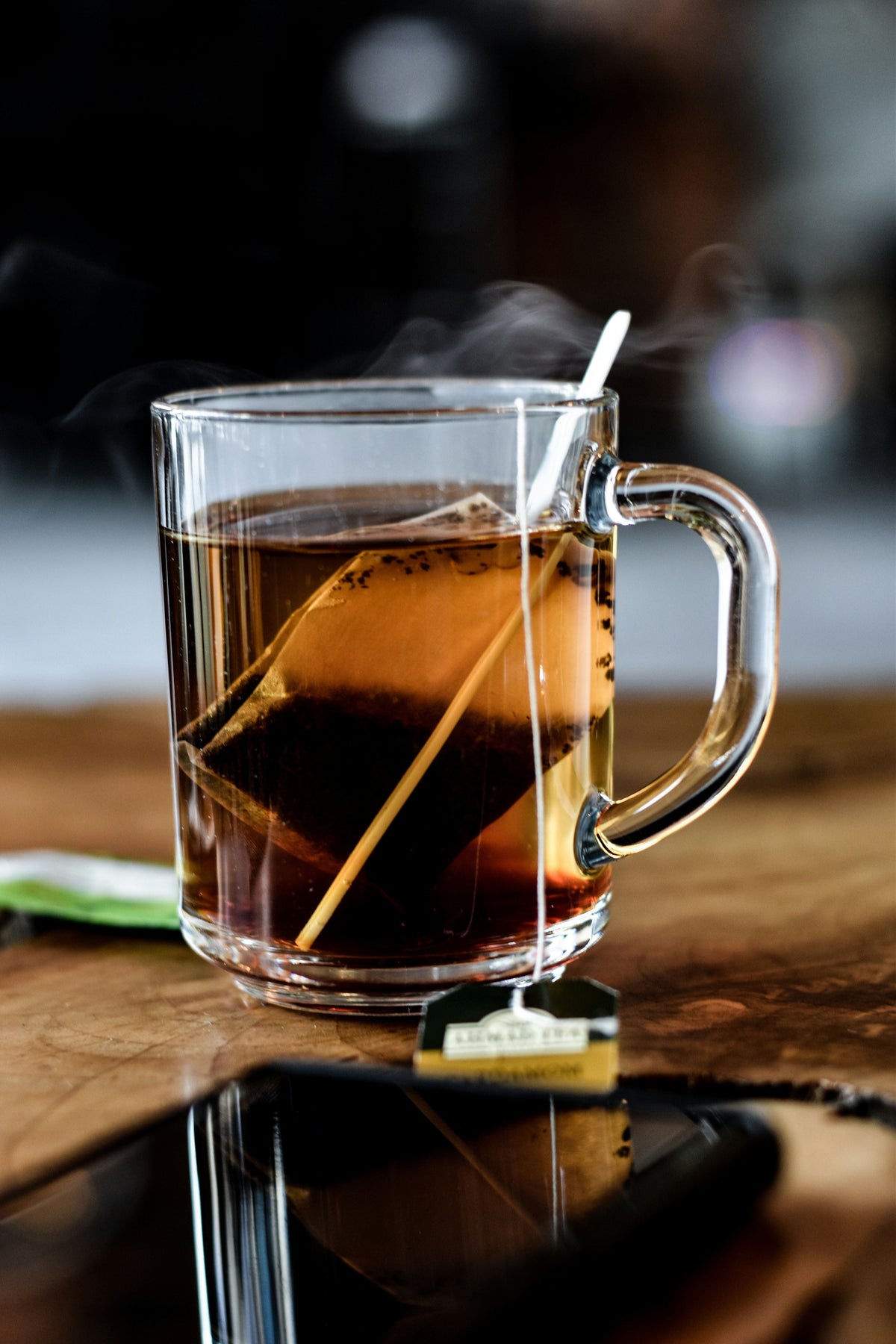 Steam rising from a glass mug of tea on a wooden table