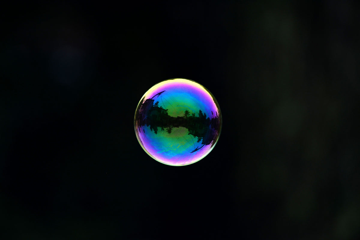 An iridescent soap bubble reflecting trees and buildings against a dark background